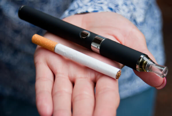 Qual a diferença entre o cigarro e o vape? mão segurando um vaper e um cigarro